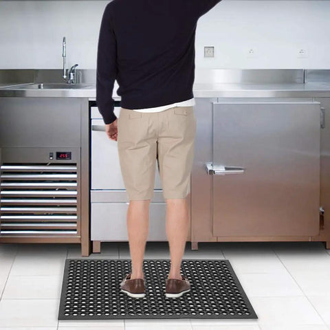 Person standing on Grippy Non Slip Rubber Drainage Floor Mat With Holes 24x36 Anti Fatigue Cushion in industrial kitchen.