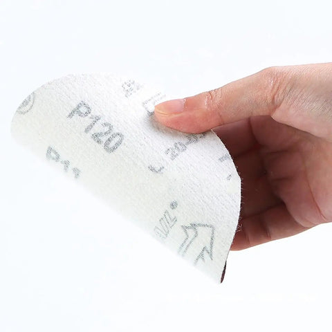 A person holding a P120 aluminum oxide sanding disc from Grab These 100-Piece Hook And Loop Sanding Discs That Pack A Punch.