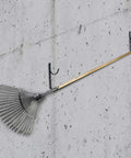 Two Pack Heavy Duty Black Aluminum Pool Pole Hangers With Screws holding garden rake on concrete wall