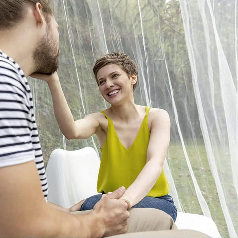 Couple seated outdoors near mosquito net bed canopy with princess lace, white four corner support, fits various sizes, single side opening.