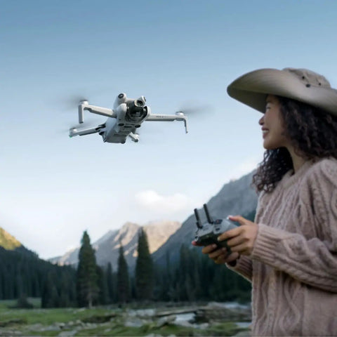 Pro Edition Mini 4 Pro Quadcopter Drone With RC 2 Controller, 4K Ultra HD Video, in flight outdoors controlled by person wearing hat