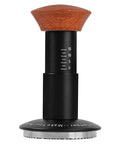 Heavy Hitter Spring Loaded Coffee Tamper With Precision Distribution Leveler And Clear Pressure Scale For Flawless Espresso Pucks featuring black stainless base and wooden handle.