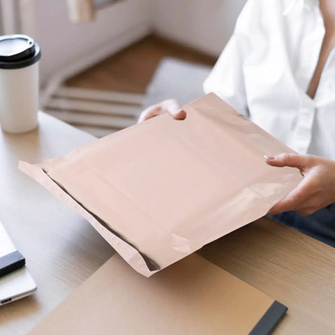 Person holding khaki mailer from 100 Pack Khaki PE Waterproof Packaging Bags With Easy Seal Closure For Clothes Cosmetics And Shipping Needs Tough As Nails Tear Resistant Heavy Duty Mail Envelopes That Keep Items Safe And Packed on table.