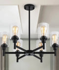 Black Farmhouse Chandelier With Six Clear Glass Shades Hanging Over Dining Table Featuring Sturdy Metal Frame And Sleek Modern Design That Hits Different for a stylish interior accent.