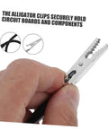 Close-up of hand using alligator clamp soldering helper set with magnifying glass lamp for secure workholding in circuit board repair.