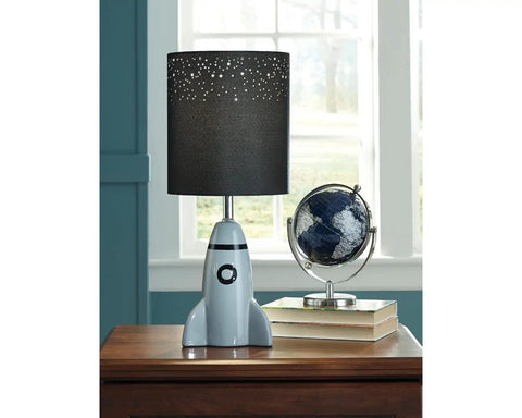 Kids Rocket Table Lamp With Gray Ceramic Base And Fabric Drum Shade on wooden desk beside globe and books by window.