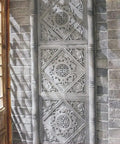 Ornate stone panel with intricate carvings set against a brick wall with a wooden door on the side.
