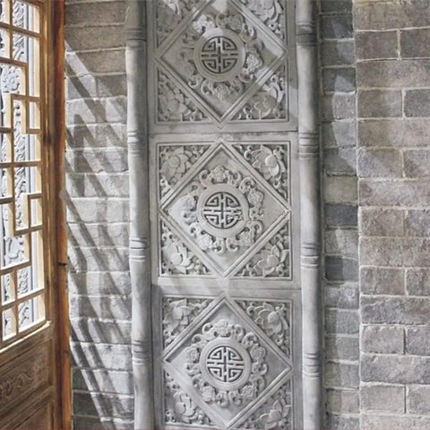 Ornate stone panel with intricate carvings set against a brick wall with a wooden door on the side.