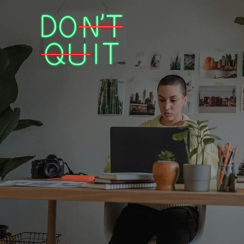 Motivational green LED neon sign 'DON'T QUIT' in a home office.
