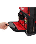 Heavy Duty Canvas Jobsite Backpack With 48 Pockets And Ultra Comfortable Load Bearing Harness Built Like A Tank For Real Deal Contractors And Crew Chiefs Who Want Solid Boss Gear On The Road, showing a hand placing a phone in the front pocket.