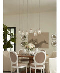 Dining room with horseshoe art, white chairs around wooden table, elegant hanging lights above for Topsail Three Light Inverted Pendant in Polished Chrome.