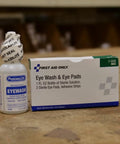 First Aid Only eye wash kit bottle and box; white bottle with blue label and tamper seal, box reads Eye Wash & Eye Pads.