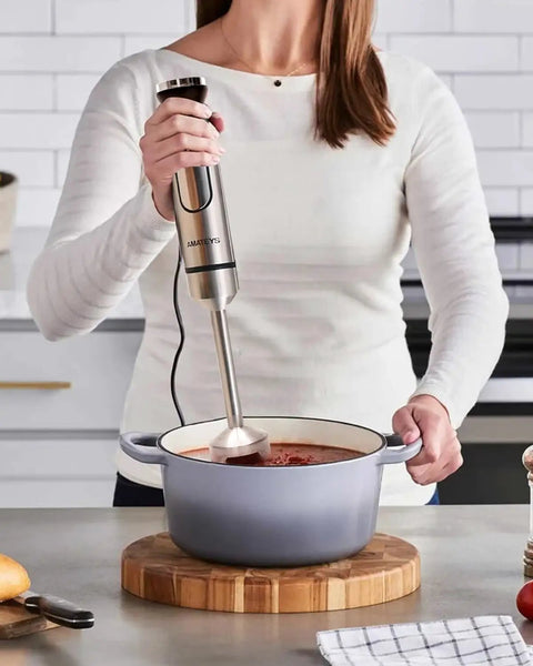 Woman using Powerful Handheld Immersion Blender 700W With Infinite Variable Speeds All In One Stainless Steel Stick Mixer to blend soup in a pot.