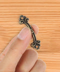 Hand holding mini antique bronze pull from 20-Piece Mini Antique Bronze Cabinet Pulls Set For Jewelry Boxes And Small Drawers.