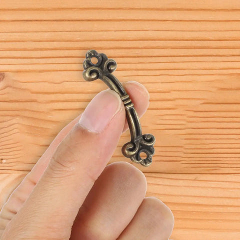 Hand holding mini antique bronze pull from 20-Piece Mini Antique Bronze Cabinet Pulls Set For Jewelry Boxes And Small Drawers.