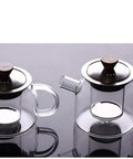 Two transparent glass teapots with stainless steel lids on a reflective surface