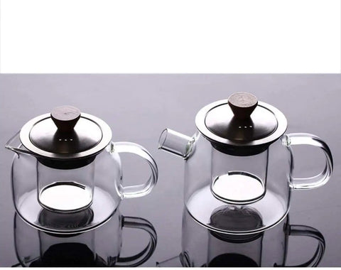 Two transparent glass teapots with stainless steel lids on a reflective surface