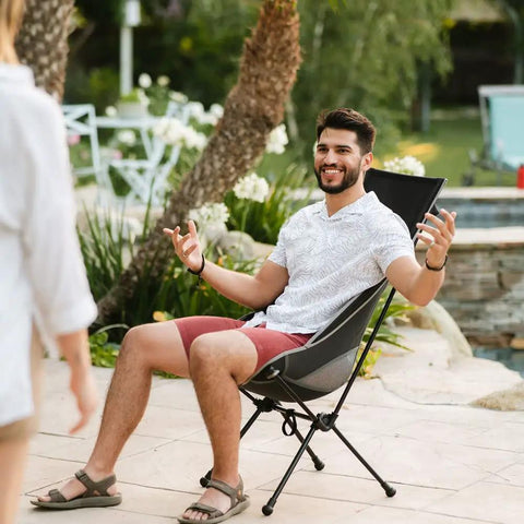 Man sitting on Chillin Chair Ultra Lightweight Foldable Portable Outdoor Seat For Tailgating Camping Backyard Barbecues And More Comfortable Durable Easy Setup Go To Seat For Family Trips Picnics And Adventures by a poolside.