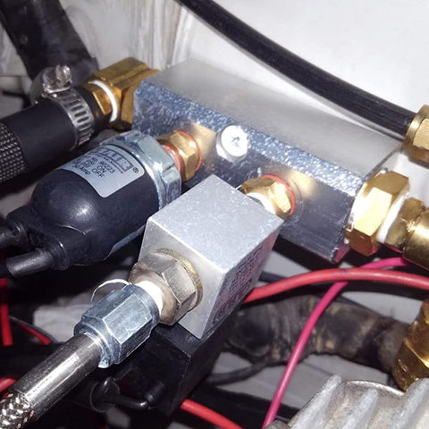Close-up of two way pneumatic manifold air distribution block with G1/2 inlet ports and G1/4 outlet ports, installed in system.