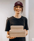 Person wearing Unisex Running Trucker Cap With Distressed Low Profile Look, holding boxes, showcasing casual hat design.