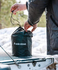 Person placing Go To Campfire Wood Burning Stove For Backpacking in a carry bag on a truck tailgate outdoors.