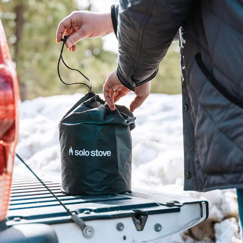 Person placing Go To Campfire Wood Burning Stove For Backpacking in a carry bag on a truck tailgate outdoors.