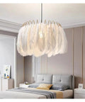 Feather Lamp Pendant Light Chandelier for Dining Room Living Bedroom Nordic Drop Lighting above a modern gray bed with gold details.