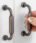 Give Your Cabinets A Serious Glow Up With These Heavy Duty 3 Inch Pulls In Smooth Oil Rubbed Bronze, showing a hand grasping a metal handle.