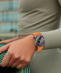 Smartwatch with orange strap on wrist, outdoors.