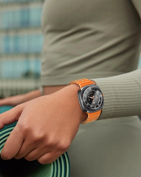 Smartwatch with orange strap on wrist, outdoors.