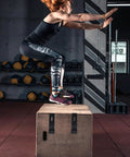 Person performing box jump in gym setting with workout equipment in background