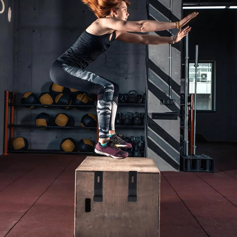 Person performing box jump in gym setting with workout equipment in background