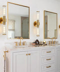 Modern bathroom with brass fixtures and white vanity, mirrors flanked by wall lights.