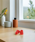 Red rubber caps on wooden desk near window with plants and vases in background