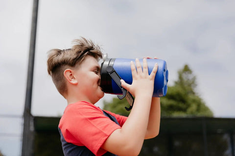 Child drinking from Half-Gallon Pro Blue Beverage Cooler With Secure Flip Cap, Wide Mouth For Easy Pouring And Fast Chug, outdoors.