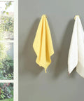 Top Shelf Brass Wall Hooks For Towels And Mugs No Sweat Rust Proof Bathroom Hanger holding yellow and white towels on gray wall.