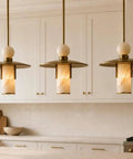 Modern Brass Pendant Chandelier Light Fixture with Alabaster Cylinder Shade Luxury Natural Stone Hanging Ceiling Light with Spherical Marble Accent for Kitchen Dining Room, Bar & Living Room Set of 3 in a cozy kitchen setting.