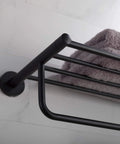 Close-up of Elie Matte Black Bathroom Shelf With Towel Bar Built Tough From Solid Brass, mounted on a bathroom wall with gray towel.