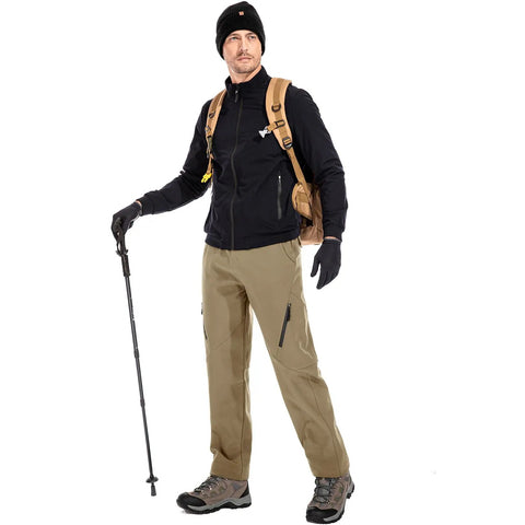 Man wearing mens waterproof hiking pants with fleece lined insulated soft shell for winter, standing with backpack and hiking stick.