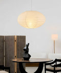 FEHEED 16 Inch Oval Plug in Hanging Paper Lantern Lights with Cord illuminating a modern dining area with dark table and sculpture.