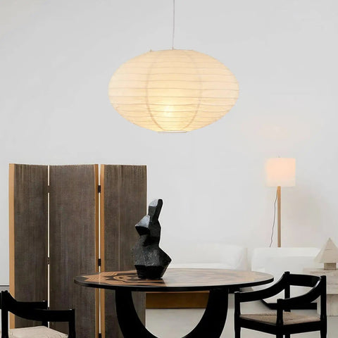 FEHEED 16 Inch Oval Plug in Hanging Paper Lantern Lights with Cord illuminating a modern dining area with dark table and sculpture.