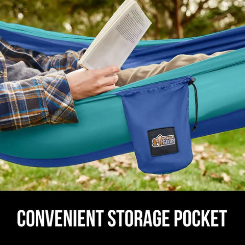 Durable Camping Hammock Built Tough With Heavy Duty Tree Straps Holds Up To 500 Lbs Steel Carabiners For A Secure Hang Easy Setup For Outdoor Trips Hiking And Backpacking Double Size Portable Blue with attached storage pocket in use outdoors.