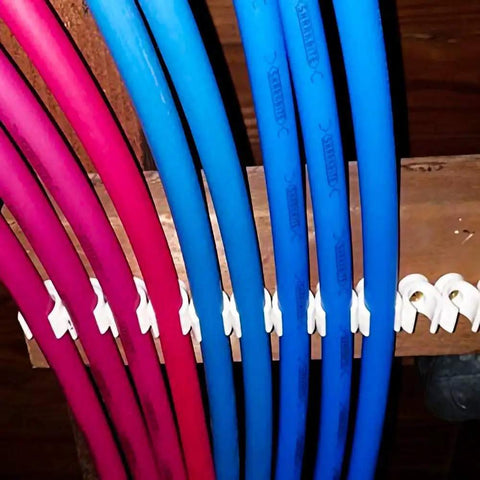 1 Inch PEX Pipe Support Hangers Set Of 130 U Hook PVC Clamps securing blue and red pipes to wooden beam
