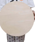 Front view of an 18-inch round unfinished plywood board with smooth surface, held by hands for crafts.