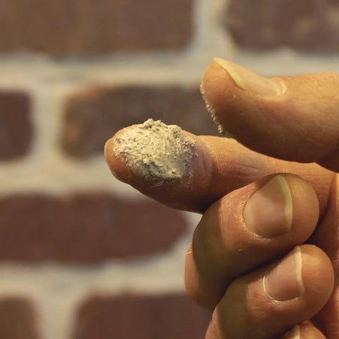 Close-up of finger with beige Top Shelf Textured Caulk Sealant For Mortar Stucco Repair On Brick Stone Concrete Masonry.