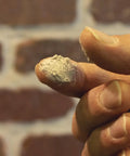 Gray Mortar And Stucco Repair Caulk 3 Pack 10.5 Oz No Hassle Squeeze Tube showing a fingertip with caulk residue against a brick wall.
