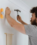 Man using Portable Screw Finder Magnetic Detector for Wood and Metal Studs to locate screw in wall before hammering.