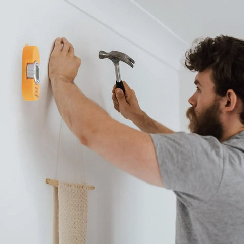 Man using Portable Screw Finder Magnetic Detector for Wood and Metal Studs to locate screw in wall before hammering.