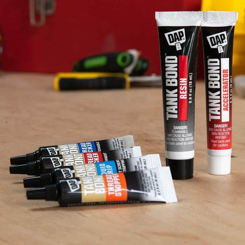 Tubes of Tank Bond Resin and Accelerator on a workbench, with two small black-and-blue labeled tubes in the foreground.