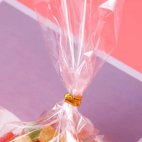 Close-up of clear 4x6 cellophane bags with 4 inch twist ties, 100 pack, tied with gold tie, filled with colorful candies.